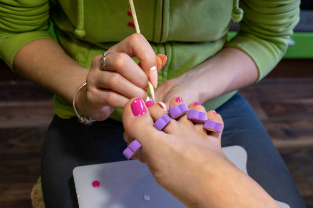 Person applying white nail polish to toenails with pink polish, using a brush and toe separators; relaxed and focused atmosphere in a beauty salon